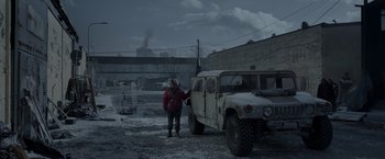 Movie still from “Black Crab” (2022), directed by Adam Berg – A man standing next to an off - road vehicle; Wide shot, Low angle