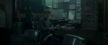 Movie still from “Black Crab” (2022), directed by Adam Berg – A man sitting at a desk in front of a computer monitor; Medium shot, Low angle