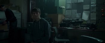 Movie still from “Black Crab” (2022), directed by Adam Berg – A man sitting in a chair in front of a desk; Medium shot, Over the shoulder angle