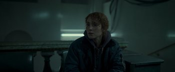 Movie still from “Black Crab” (2022), directed by Adam Berg – A woman sitting down in a dark room; Close Up shot, Over the shoulder angle