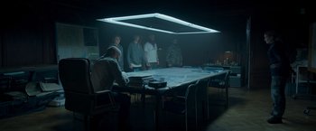 Movie still from “Black Crab” (2022), directed by Adam Berg – A group of people standing around a large table; Wide shot, Over the shoulder angle