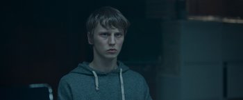 Movie still from “Black Crab” (2022), directed by Adam Berg – A young man in a hooded sweatshirt looks at the camera; Close Up shot, Over the shoulder angle