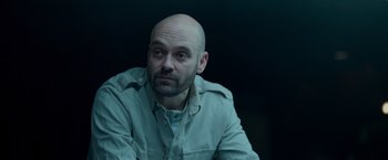 Movie still from “Black Crab” (2022), directed by Adam Berg – A man with a bald head sitting in front of a black background; Close Up shot, Over the shoulder angle