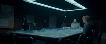 Movie still from “Black Crab” (2022), directed by Adam Berg – A man sitting at a table in a dark room; Wide shot, High angle