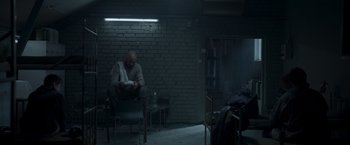 Movie still from “Black Crab” (2022), directed by Adam Berg – A man sitting on a chair in a dark room; Wide shot, High angle