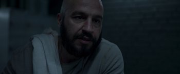 Movie still from “Black Crab” (2022), directed by Adam Berg – A bald man with a beard is sitting in a dark room; Close Up shot, Low angle