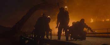 Movie still from “Black Crab” (2022), directed by Adam Berg – A group of people standing in front of a burning building; Wide shot, Low angle