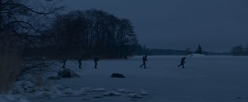 Movie still from “Black Crab” (2022), directed by Adam Berg – A group of people walking across a snow covered field; Extreme Wide shot, Low angle