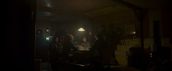 Movie still from “Black Crab” (2022), directed by Adam Berg – A group of people sitting at a table in a dark room; Wide shot, Low angle