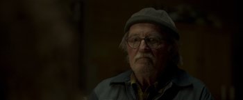 Movie still from “Black Crab” (2022), directed by Adam Berg – An older man wearing glasses and a hat; Close Up shot, Over the shoulder angle