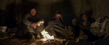 Movie still from “Black Crab” (2022), directed by Adam Berg – Two people sitting in the dark next to a fire; Medium shot, High angle