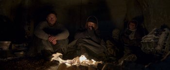 Movie still from “Black Crab” (2022), directed by Adam Berg – A man and a woman sitting next to each other in front of a fire; Wide shot, High angle