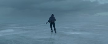 Movie still from “Black Crab” (2022), directed by Adam Berg – A person walking in the water holding a gun; Extreme Wide shot, High angle