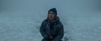 Movie still from “Black Crab” (2022), directed by Adam Berg – A person sitting on the ground in the snow; Medium shot, High angle