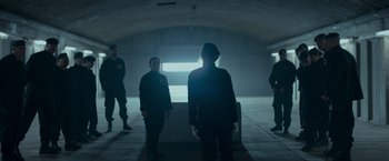 Movie still from “Black Crab” (2022), directed by Adam Berg – A group of men standing in a dark room; Wide shot, Over the shoulder angle