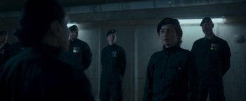 Movie still from “Black Crab” (2022), directed by Adam Berg – A group of people standing next to each other in a room; Medium shot, Over the shoulder angle