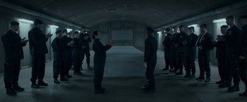 Movie still from “Black Crab” (2022), directed by Adam Berg – A group of people standing around in a room; Wide shot, High angle