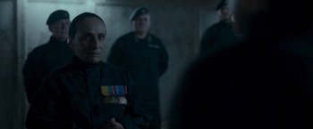 Movie still from “Black Crab” (2022), directed by Adam Berg – A group of men standing next to each other in a room; Close Up shot, Over the shoulder angle