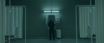 Movie still from “Black Crab” (2022), directed by Adam Berg – A person standing in a room next to a mirror; Wide shot, Low angle