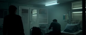 Movie still from “Black Crab” (2022), directed by Adam Berg – A man sitting on a chair in a dark room; Wide shot, Over the shoulder angle