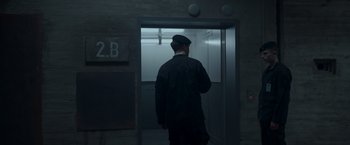 Movie still from “Black Crab” (2022), directed by Adam Berg – A man standing in front of an open door of an elevator; Wide shot, Low angle