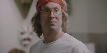 Movie still from “BlackBerry” (2023), directed by Matt Johnson – A man wearing glasses and a red headband; Close Up shot, Over the shoulder angle