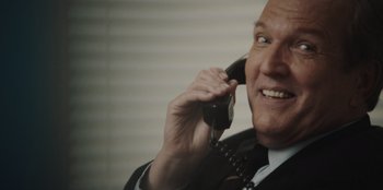 Movie still from “BlackBerry” (2023), directed by Matt Johnson – An older man talking on a phone while wearing a suit and tie; Close Up shot, Over the shoulder angle
