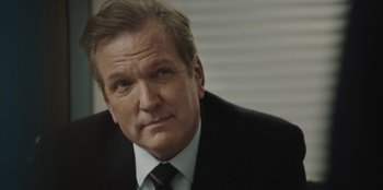 Movie still from “BlackBerry” (2023), directed by Matt Johnson – An older man in a suit and tie looking at the camera; Close Up shot, Over the shoulder angle