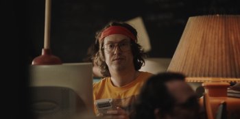 Movie still from “BlackBerry” (2023), directed by Matt Johnson – A man with a red headband is holding a nintendo wii controller; Close Up shot, Low angle