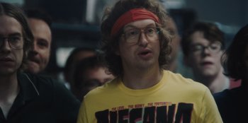 Movie still from “BlackBerry” (2023), directed by Matt Johnson – A man in a yellow t - shirt and a red head band; Close Up shot, Over the shoulder angle