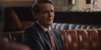 Movie still from “BlackBerry” (2023), directed by Matt Johnson – A man in a suit and tie sitting in a chair; Close Up shot, Over the shoulder angle