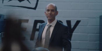 Movie still from “BlackBerry” (2023), directed by Matt Johnson – A man in a suit and tie standing in front of a wall; Medium shot, Low angle
