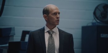 Movie still from “BlackBerry” (2023), directed by Matt Johnson – A man in a suit and tie standing in front of a wall; Close Up shot, Low angle