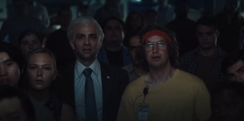 Movie still from “BlackBerry” (2023), directed by Matt Johnson – A man and a woman standing next to each other in front of a group of people; Medium shot, Low angle