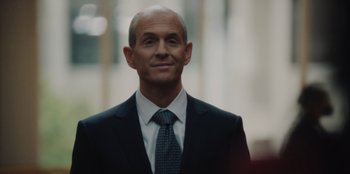 Movie still from “BlackBerry” (2023), directed by Matt Johnson – A man in a suit and tie smiling for the camera; Close Up shot, Over the shoulder angle