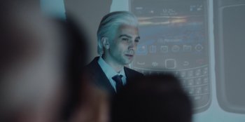 Movie still from “BlackBerry” (2023), directed by Matt Johnson – A man in a suit and white hair looks at a projector screen; Close Up shot, Over the shoulder angle
