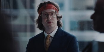 Movie still from “BlackBerry” (2023), directed by Matt Johnson – A man in a suit and tie wearing a head band; Close Up shot, Low angle