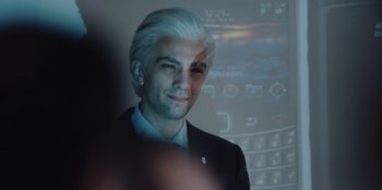 Movie still from “BlackBerry” (2023), directed by Matt Johnson – A man in a suit and white hair is smiling for the camera; Close Up shot, Over the shoulder angle