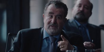 Movie still from “BlackBerry” (2023), directed by Matt Johnson – An older man wearing a suit and tie; Close Up shot, Over the shoulder angle