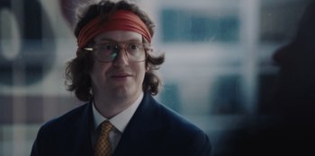 Movie still from “BlackBerry” (2023), directed by Matt Johnson – A man wearing a red head band and a suit; Close Up shot, Over the shoulder angle