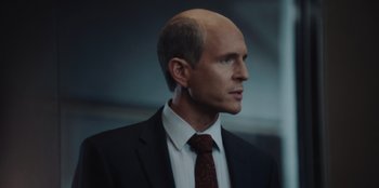 Movie still from “BlackBerry” (2023), directed by Matt Johnson – A man in a suit and tie looking to his left; Close Up shot, Over the shoulder angle