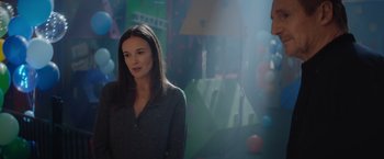 Movie still from “Blacklight” (2022), directed by Mark Williams – A woman standing in front of a wall with balloons; Medium shot, Over the shoulder angle