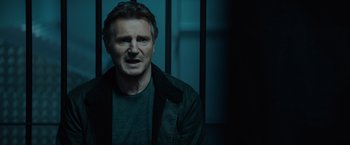 Movie still from “Blacklight” (2022), directed by Mark Williams – A man in a black jacket is standing in front of a window; Close Up shot, Over the shoulder angle