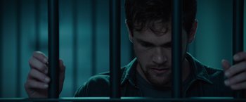 Movie still from “Blacklight” (2022), directed by Mark Williams – A person behind bars in a room; Close Up shot, Low angle