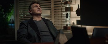 Movie still from “Blacklight” (2022), directed by Mark Williams – A man sitting on a couch looking up at the sky; Medium shot, Over the shoulder angle