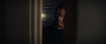 Movie still from “Blacklight” (2022), directed by Mark Williams – A man standing in a dark room looking at the camera; Close Up shot, Low angle