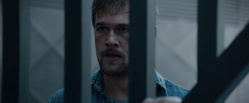Movie still from “Blacklight” (2022), directed by Mark Williams – A person behind a metal fence; Close Up shot, Over the shoulder angle