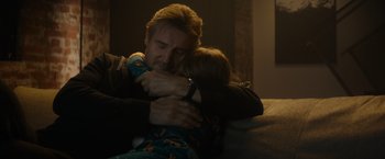 Movie still from “Blacklight” (2022), directed by Mark Williams – A man and a child hugging on a couch; Close Up shot, Low angle