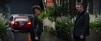 Movie still from “Blacklight” (2022), directed by Mark Williams – A woman in a leather jacket standing on the sidewalk; Wide shot, Over the shoulder angle