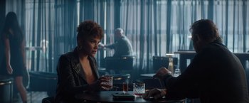 Movie still from “Blacklight” (2022), directed by Mark Williams – A woman sitting at a table with a glass of wine; Medium shot, Over the shoulder angle